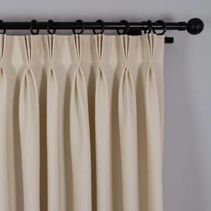 May include: A set of off-white curtains with pleats hanging from a black curtain rod.