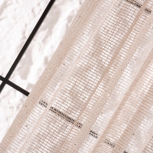May include: A close-up of a sheer beige curtain with a geometric pattern and small, shiny beads. The curtain is made of a delicate, lightweight fabric and has a subtle shimmer.