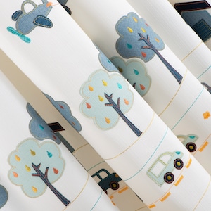 May include: White fabric with blue, green, and yellow embroidered trees, cars, and airplanes. The fabric has a subtle texture.