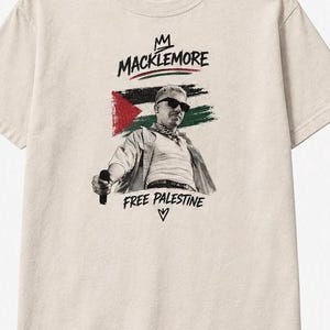 May include: A beige short-sleeve t-shirt featuring a graphic print of Macklemore wearing sunglasses and a bandana. Behind the figure is a stylized Palestinian flag. The text MACKLEMORE appears above, and FREE PALESTINE with a heart symbol below.