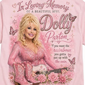 May include: A light pink t-shirt featuring a graphic of Dolly Parton with blonde hair, wearing a pink outfit, and holding a guitar. The text reads In Loving Memory of a Beautiful Soul, Dolly Parton, If you want the rainbow, you gotta put up with the rain, Forever in our hearts, and Thank you for the music, the laughter & the love, surrounded by pink butterflies and roses.