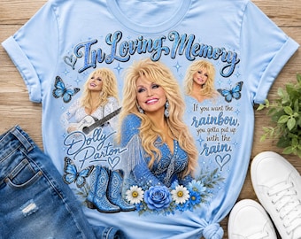 May include: A light blue t-shirt featuring a graphic print of Dolly Parton with the text In Loving Memory, Dolly Parton, and If you want the rainbow, you gotta put up with the rain. The design includes blue butterflies, blue boots, and flowers.