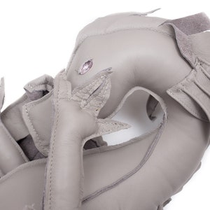 May include: A gray leather dragon toy with a pink gem for an eye. The dragon is curled up with its tail in its mouth.