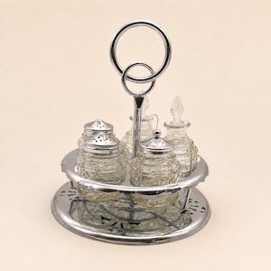 May include: A silver-toned metal condiment caddy featuring a circular handle and a decorative base. The set includes four clear glass containers with textured patterns, two with perforated silver lids and two with clear glass stoppers.