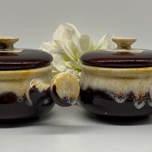 May include: Two small brown and cream ceramic soup pots with lids and handles. The pots have a glazed finish with a brown and cream swirl pattern.