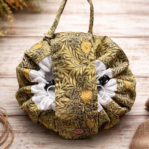 May include: A round, floral-patterned makeup bag with a handle. The bag features a yellow and green botanical design on a dark background. The interior is white with a drawstring closure. The bag is approximately 8 inches in diameter.