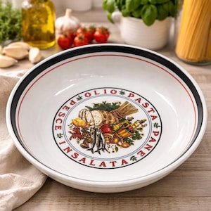 May include: White ceramic serving bowl with a black and red rim. The bowl's center features a colorful illustration of Italian food items, including bread, vegetables, and fish, with the words "OLIO PASTA PANE INSALATA PESCE" around the border.