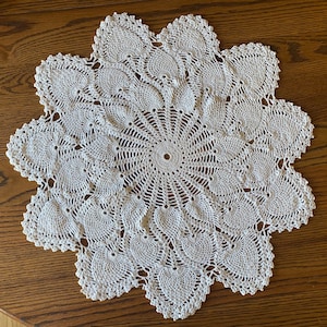 May include: A white crocheted doily with a circular design and a scalloped edge.