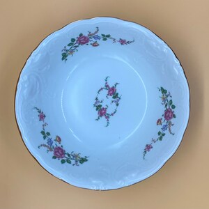 May include: White ceramic bowl with a floral design. The bowl has a scalloped edge and a gold rim. The flowers are pink, purple, and blue.