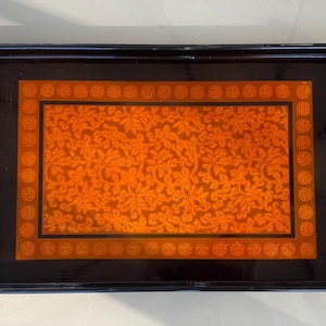 Peut inclure: Un plateau de service laqué noir avec un motif floral orange décoratif. Le plateau a deux poignées sur les côtés.