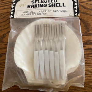 May include: A white ceramic baking shell with six silver forks, packaged in a clear plastic bag. The packaging has the text "SELECTED BAKING SHELL" and "FOR ALL TYPES OF SEAFOOD AU GRATIN DISHES."