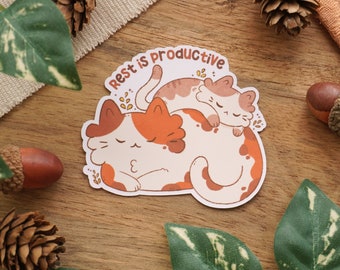 Könnte beinhalten: Ein Aufkleber mit zwei schlafenden Comic-Katzen, die übereinander liegen. Der Text "Rest is productive" ist in brauner Schrift über den Katzen geschrieben.