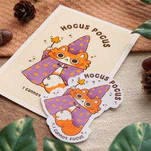 May include: Two purple and orange cat stickers with the text "Hocus Pocus" and "I cannot focus" on a brown wooden surface.