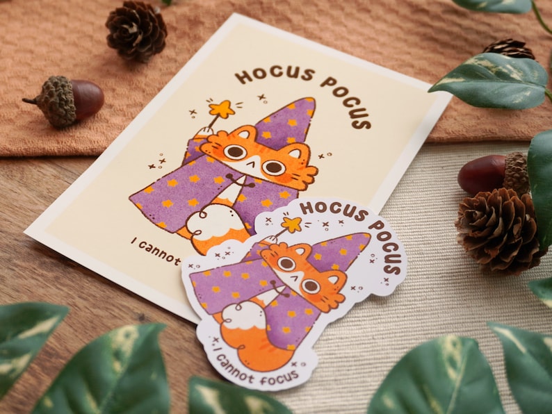May include: Two purple and orange cat stickers with the text "Hocus Pocus" and "I cannot focus" on a brown wooden surface.