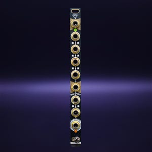 May include: A black electronic module with gold-coloured jacks and the text "MULT PERT" printed on it. The module has a series of circular jacks and indicator lights. The background is a gradient of dark blue and purple.