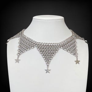 Pode incluir: Um colar choker de malha de prata com tr&ecirc;s pingentes em forma de estrela.