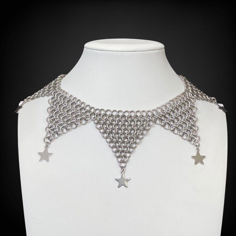 Pode incluir: Um colar choker de malha de prata com tr&ecirc;s pingentes em forma de estrela.