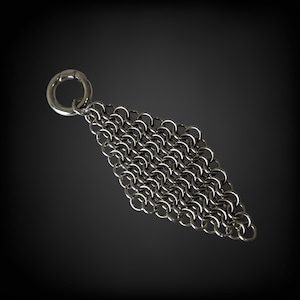 May include: A silver chainmail accessory in a diamond shape, composed of small, interlocking metal rings. A larger ring is at the top for attachment. The background is a dark grey.