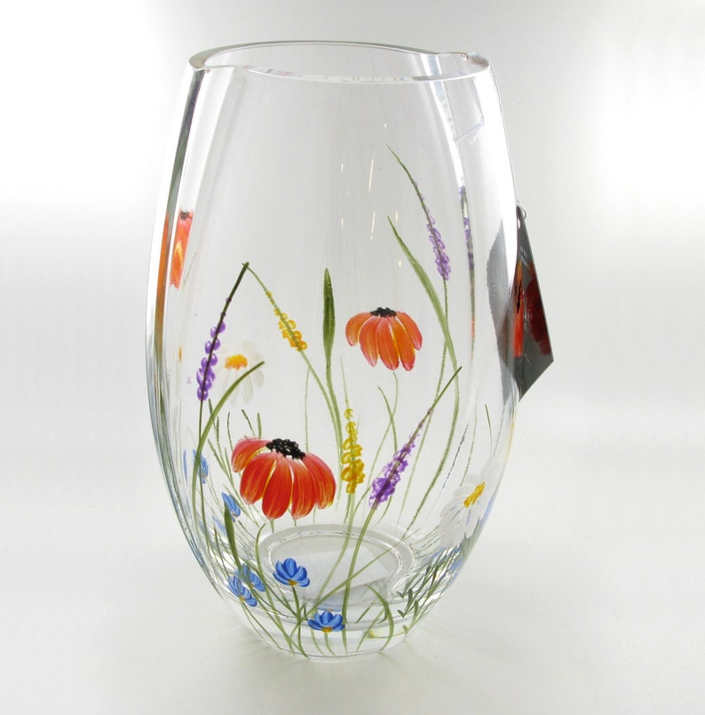 May include: A clear glass vase with a hand-painted design of colorful wildflowers. The vase has a rounded bottom and a wide opening at the top.