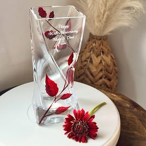May include: A clear glass vase with a twisted design and red painted leaves. The vase is engraved with the text "Happy 40th Anniversary Mum & Dad xxx".