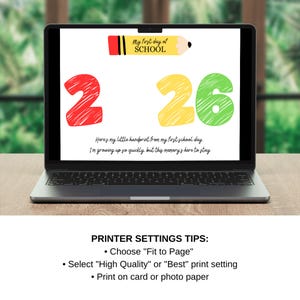 May include: A laptop displays a colorful print for a child's first day of school. The design includes a red '2', a yellow '26', and a pencil graphic with the text 'My first day of SCHOOL'. Below, text reads, 'Here's my little handprint...'.