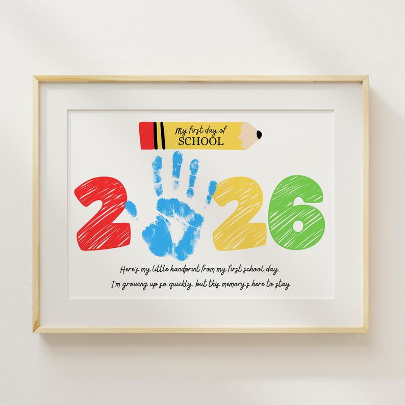 May include: Framed print with a light wood frame. The artwork features a colorful design with the text "My first day of SCHOOL" and the numbers "2 2 6". A blue handprint is in the center. The text below reads "Here's my little handprint from my first school day. I'm growing up so quickly, but this memory's here to stay."