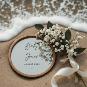 Peut inclure: Un miroir rond encadré de bois avec un fond blanc et le texte "Baby Jones August 202X" en lettres noires. Un bouquet de gypsophile blanc avec des tiges vertes et un ruban blanc sont au premier plan.