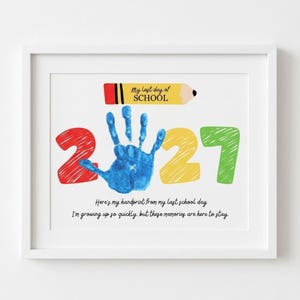 May include: A framed print featuring a yellow pencil graphic with the text My last day of SCHOOL, a red number 2, a blue handprint, a yellow number 2, and a green number 7. Below, the text reads Here's my handprint from my last school day.