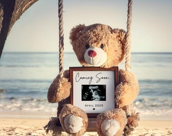 Op de afbeelding: Een pluche teddybeer op een schommel houdt een ingelijste echografie-afbeelding vast. De lijst leest "Coming Soon..." en "April 2025". De beer is lichtbruin met een rode neus, tegen een strand- en oceaanachtergrond.