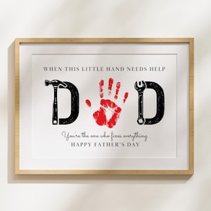 Könnte beinhalten: Gerahmter Kunstdruck mit dem Wort "DAD", gebildet aus einem Hammer, einem roten Handabdruck und einem Schraubenschlüssel. Der Text lautet "Wenn diese kleine Hand Hilfe braucht" und "Du bist derjenige, der alles repariert. Fröhlichen Vatertag."