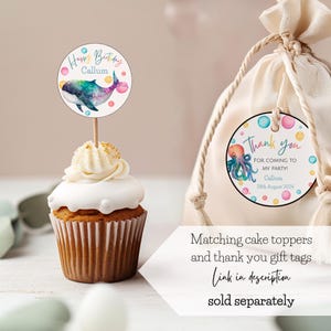 K&ouml;nnte beinhalten: Ein Cupcake mit wei&szlig;em Zuckerguss und einem Tortenaufleger mit einem Aquarellwal-Design. Eine Geschenkt&uuml;te mit einem Anh&auml;nger mit der Aufschrift "Danke" und einer Oktopus-Illustration. Der Text auf dem Bild lautet "Happy Birthday Callum" und "F&uuml;r das Kommen zu meiner Party!"