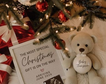Può includere: Annuncio natalizio con un orsacchiotto all'uncinetto che tiene un ornamento bianco con "Baby Thompson". Una lavagna luminosa mostra "The Most Special Christmas Gift Is On The Way" con un'immagine ecografica. Regali rossi e un albero di Natale sullo sfondo.