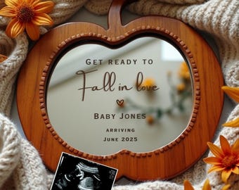 May include: Wooden apple-shaped mirror with a message that reads "Get ready to Fall in love" with a heart and the text "Baby Jones Arriving June 2025". A black and white ultrasound image is placed in front of the mirror.