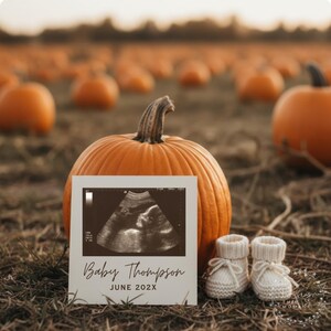 Op de afbeelding: Een oranje pompoen met een echofoto met de tekst "Baby Thompson JUNE 202X" en een paar witte babyslofjes. De foto staat voor de pompoen, met andere pompoenen op de achtergrond.