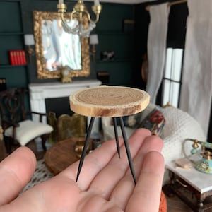 Peut inclure: Une table miniature en bois avec un plateau rond en bois naturel et trois pieds en métal noir. La table est assez petite pour tenir dans la paume de la main.