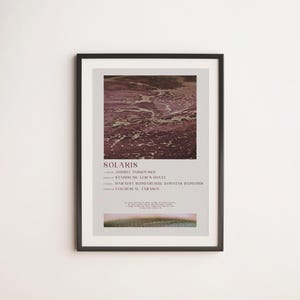 Könnte beinhalten: A framed poster with the title "SOLARIS". The poster features an abstract image in maroon and beige at the top, with text below. The black frame contrasts with the white wall on which it is displayed.