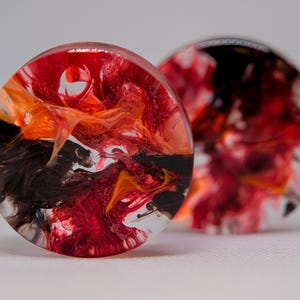 May include: Two round resin plugs with swirling patterns of red, orange, and black.