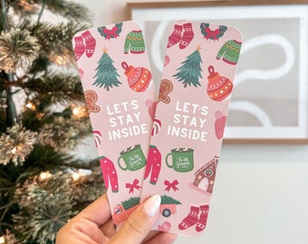 May include: Two pink Christmas-themed bookmarks with illustrations of Christmas trees, ornaments, gingerbread houses, and the text "Let's Stay Inside".