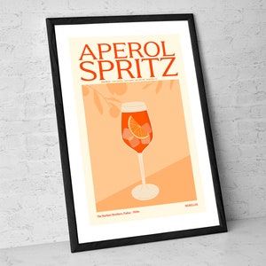 May include: A vintage-style poster featuring an illustration of an Aperol Spritz cocktail in a tall glass with an orange slice and ice cubes. The poster is on a peach background with a stylised orange tree branch in the background. The text "APEROL SPRITZ" is in bold, black letters at the top of the poster. The text "The Barbieri Brothers, Padua, 1950s" is at the bottom of the poster.