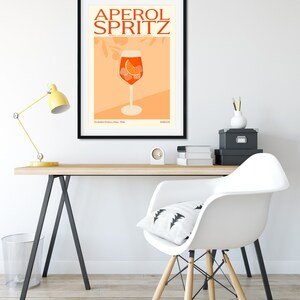 May include: A black framed poster with the text "Aperol Spritz" in orange and white. The poster features a glass of Aperol Spritz with an orange slice and ice cubes on a peach background.