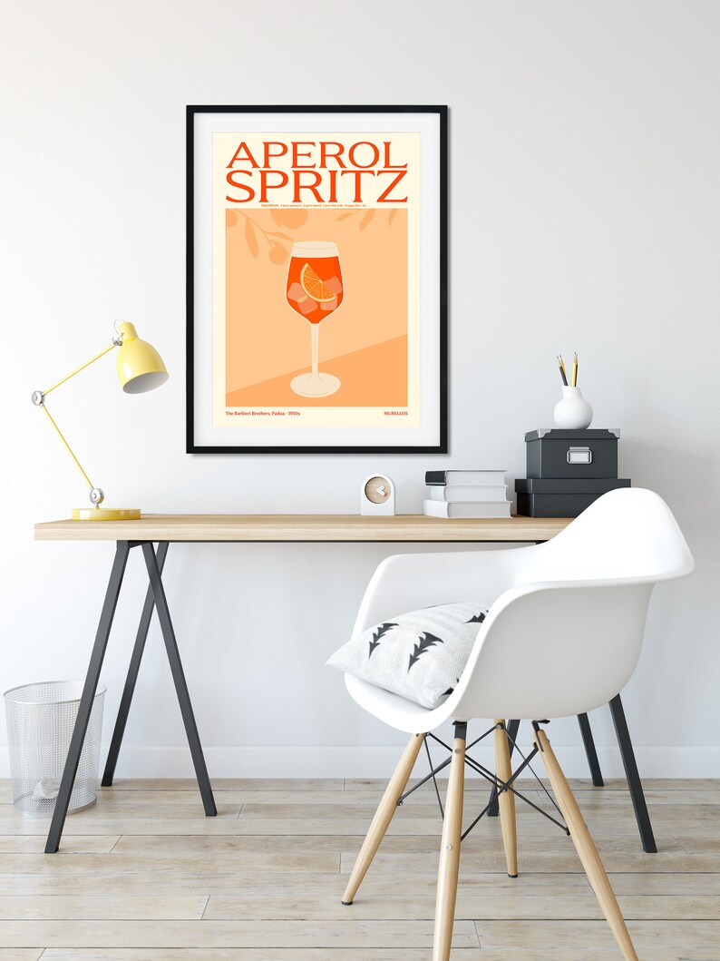 May include: A black framed poster with the text "Aperol Spritz" in orange and white. The poster features a glass of Aperol Spritz with an orange slice and ice cubes on a peach background.