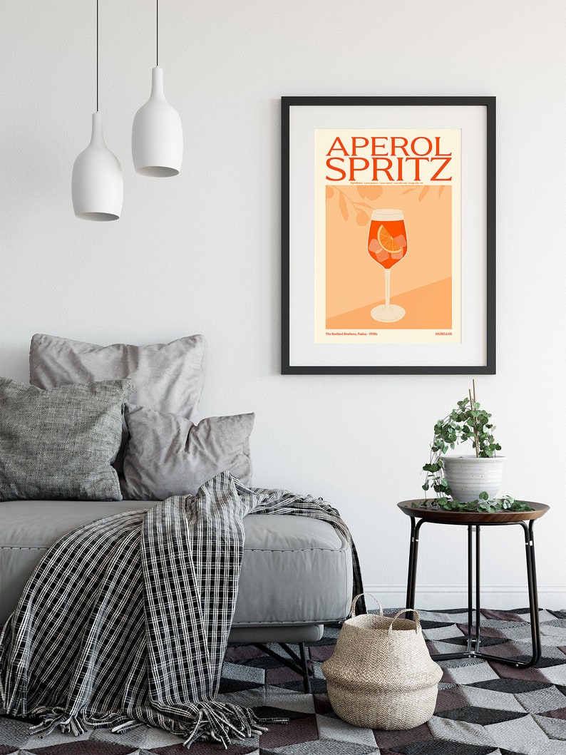 May include: A black framed poster with the text "Aperol Spritz" in red and orange letters. The poster features a glass of Aperol Spritz with an orange slice and ice cubes on a peach background.