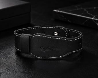 May include: A black leather bracelet featuring white contrast stitching along the edges. The band includes a single leather loop and a silver-toned metal snap button closure. The word Leatherau is embossed in a script font on the front surface.