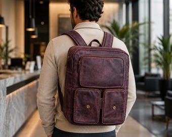 May include: A dark burgundy leather backpack with a rectangular shape, featuring one large upper zippered pocket and two smaller lower pockets with brass-colored snap closures. The bag has adjustable shoulder straps and a top carry handle.