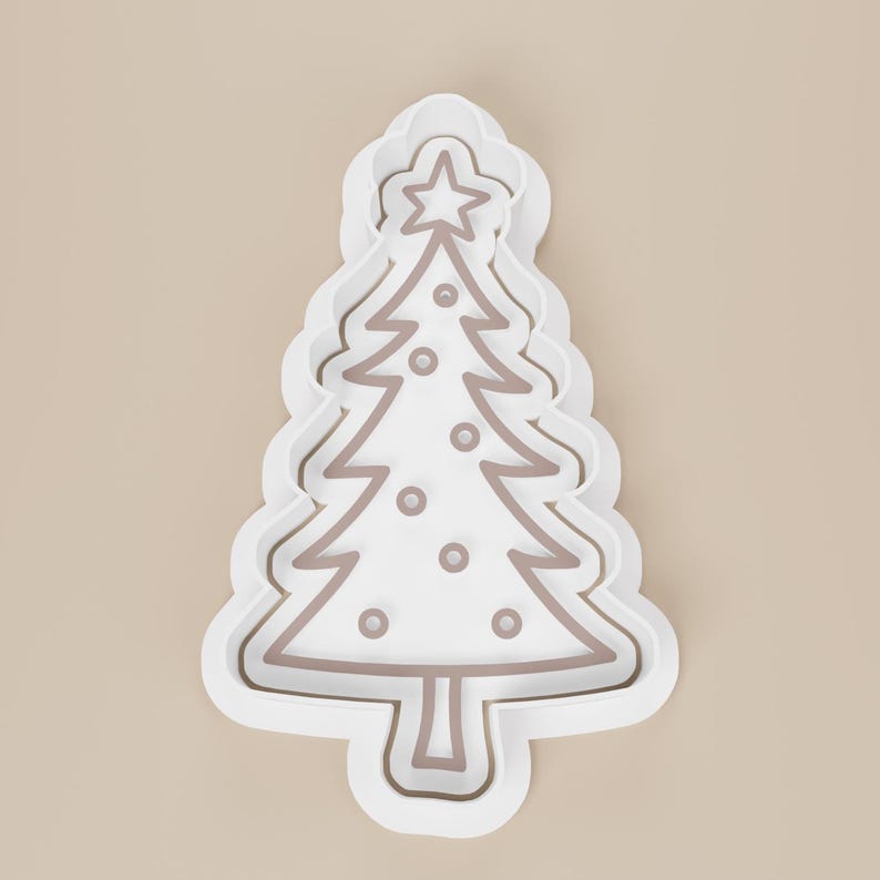 May include: A white Christmas tree cookie cutter with a brown outline and star on top. The tree has decorative circles and a scalloped edge. Perfect for holiday baking.