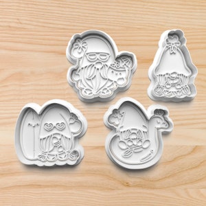 May include: Four white plastic cookie cutters shaped like gnomes in various summer-themed poses. One gnome is wearing sunglasses and holding a drink, another is holding a surfboard, another is wearing a flower crown, and the last is riding a swan float.