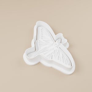 May include: A white butterfly-shaped cookie cutter. The cutter has detailed wing patterns and a rounded edge. The design is suitable for baking or crafting projects.