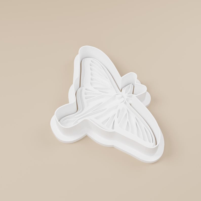 May include: A white butterfly-shaped cookie cutter. The cutter has detailed wing patterns and a rounded edge. The design is suitable for baking or crafting projects.