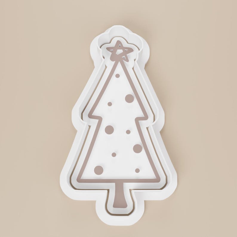 May include: A white Christmas tree-shaped cookie cutter with a star on top and decorative dots. The cutter has a layered design with a light brown interior and a white exterior.