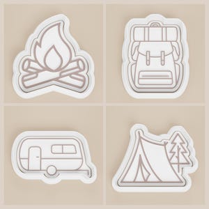 May include: Four camping-themed cookie cutters. Designs include a campfire with flames, a backpack, a travel trailer, and a tent with a tree. Each cutter has a white border and a light brown interior.